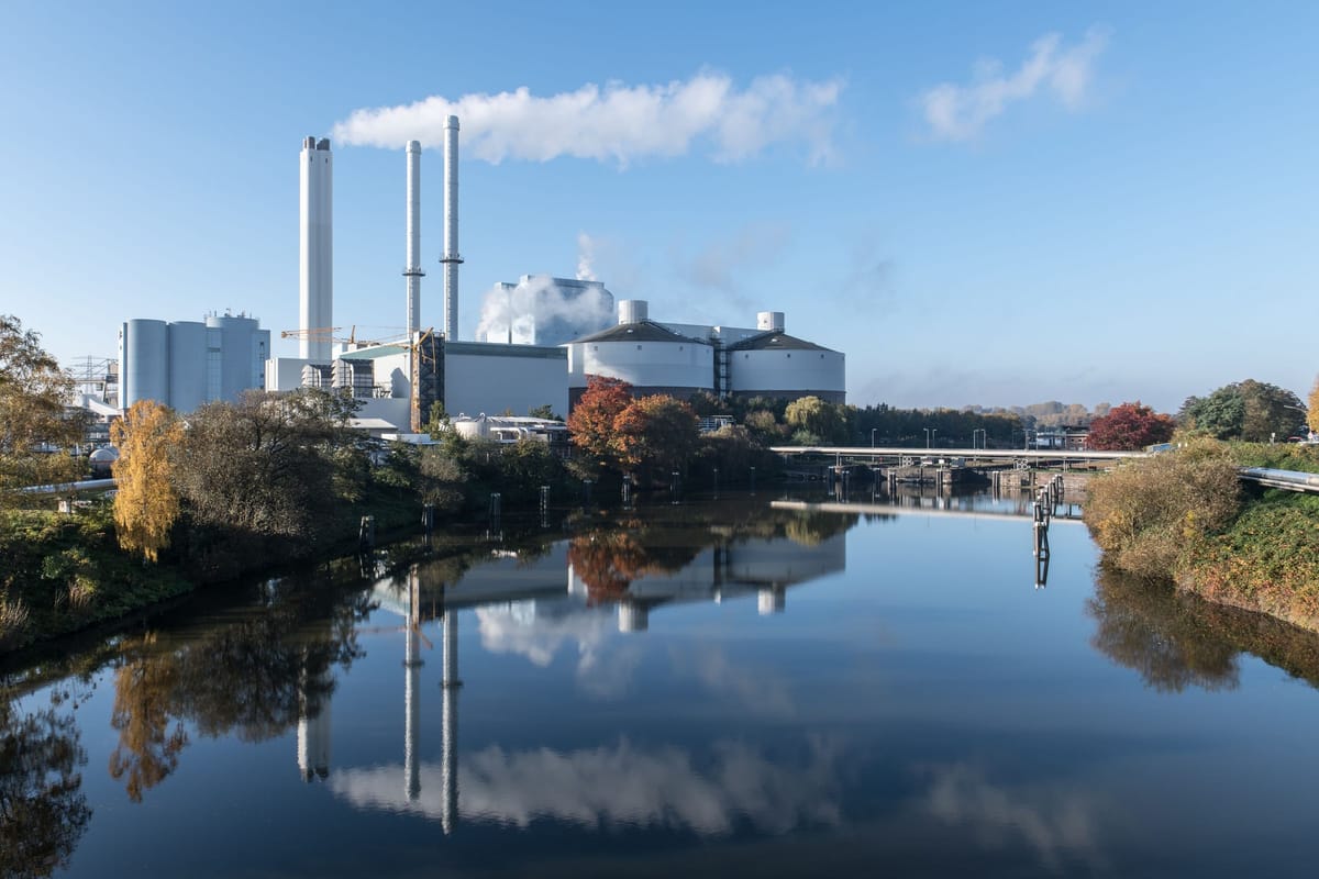 Heating plant with tall chimneys on a riverbank, reflected in the still water